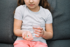 criança segurando remédios e copo de água